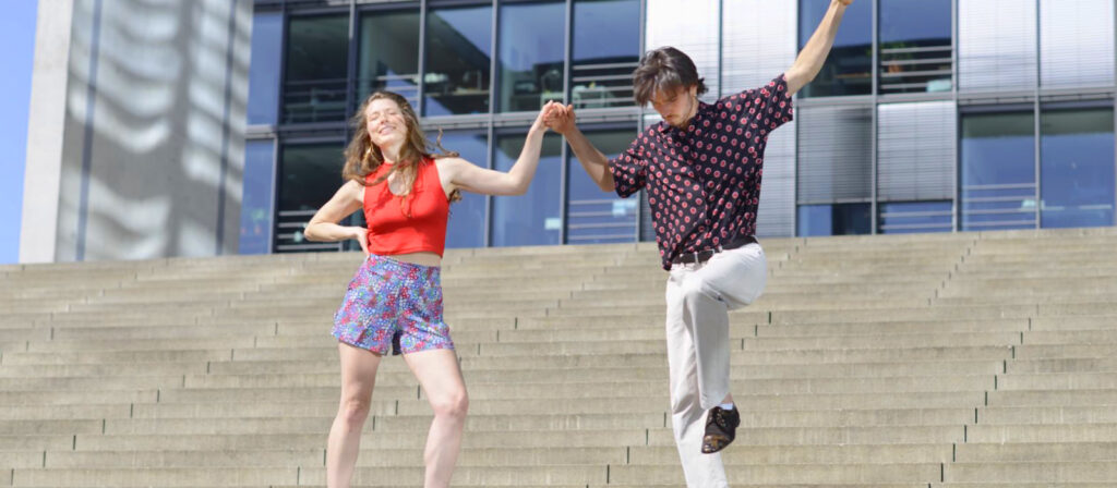 helen and yago, two dancers in open couple dance position on stairs in front of modern building